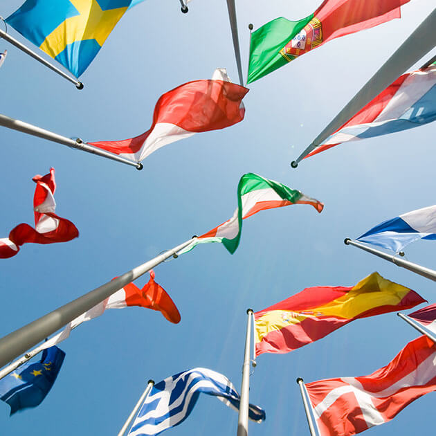 A view of various national flags waving against a bright blue sky, captured from a low angle.