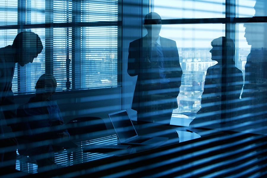 A silhouetted group of people is seen through office blinds.