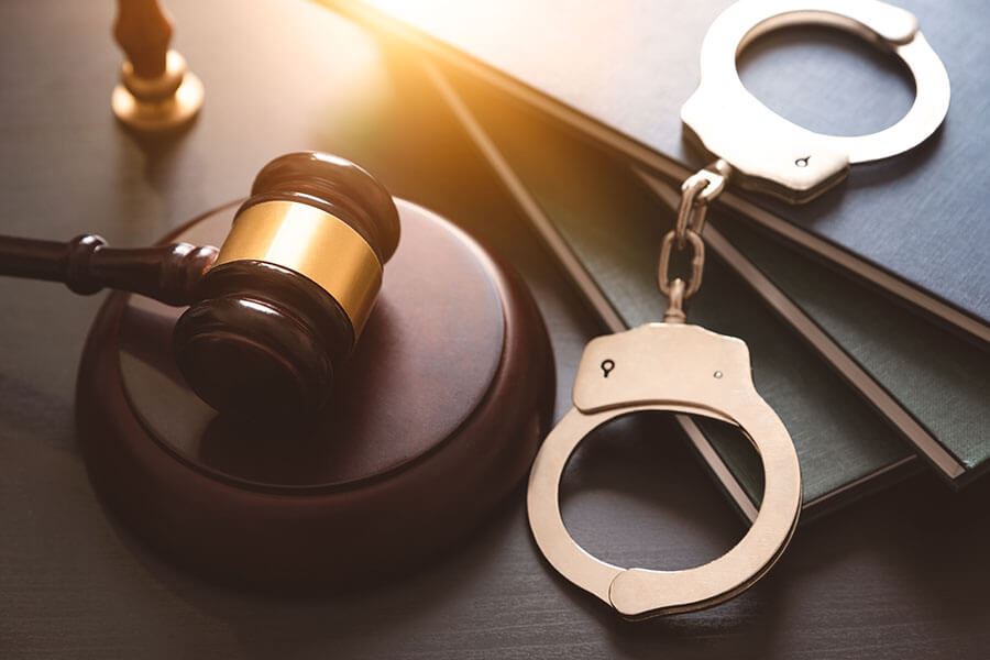 A gavel, a pair of handcuffs, a stamp and books placed on a wooden desk.