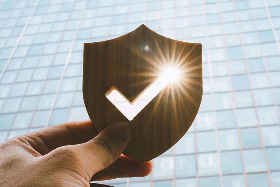 A hand holds a wooden shield in front of a glass building.