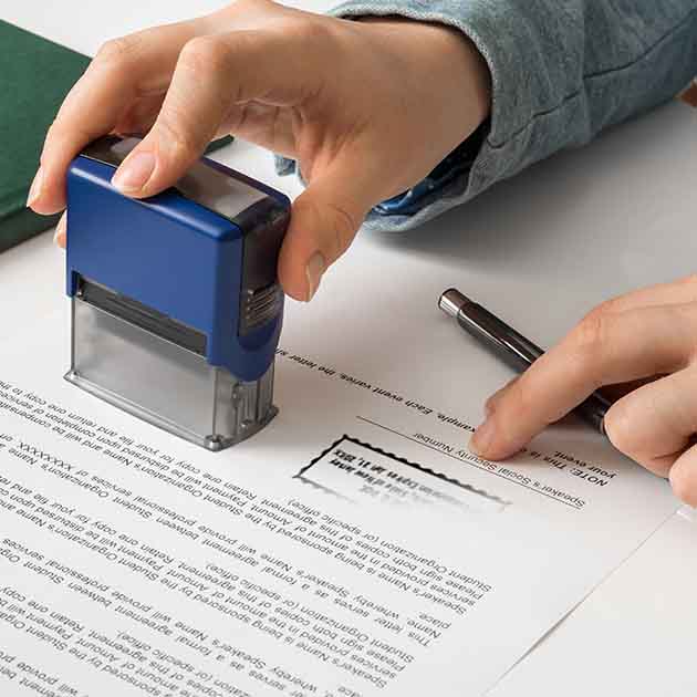 Hand pressing down on blue Notary stamp on paper document