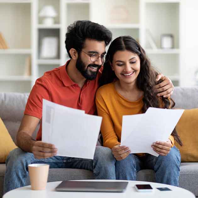 A smiling couple sitting on a couch, reviewing paperwork together.