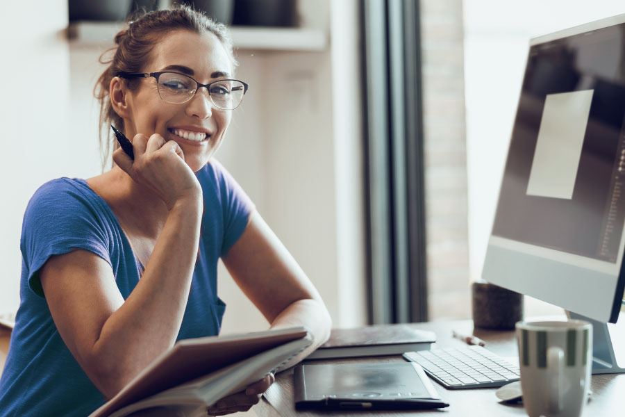 Side view of smiling Notary in casual attire and glasses at her desk with a pen and notebook in hand