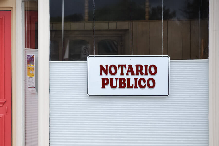 White sign reading 'NOTARIO PUBLICO' in red letters on a storefront window.